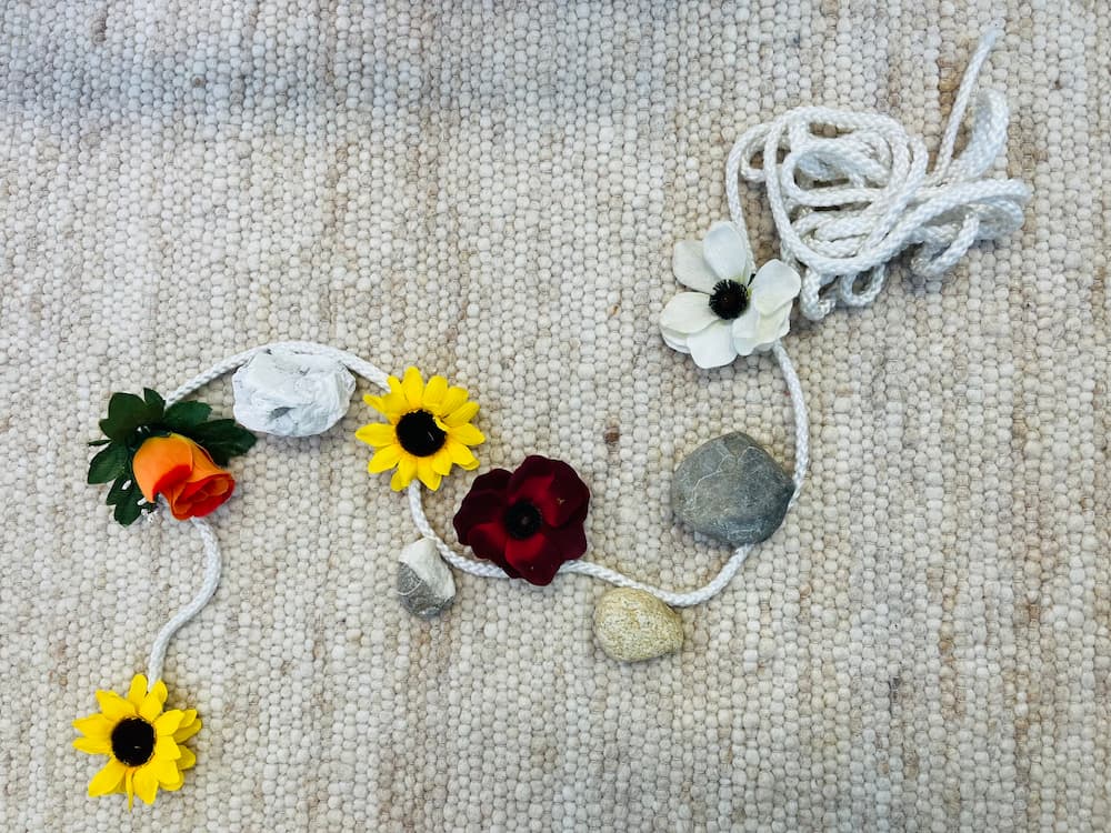 Eine beispielhafte Lifeline gelegt aus einem hellen Seil mit Blumen und Steinen zum Symbolisieren von Ereignissen in der Lebensgeschichte.